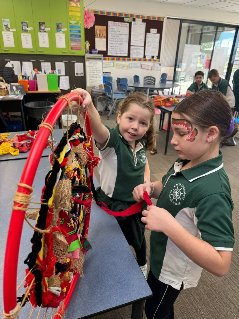 Two students weaving fabric strips through a hoop in class