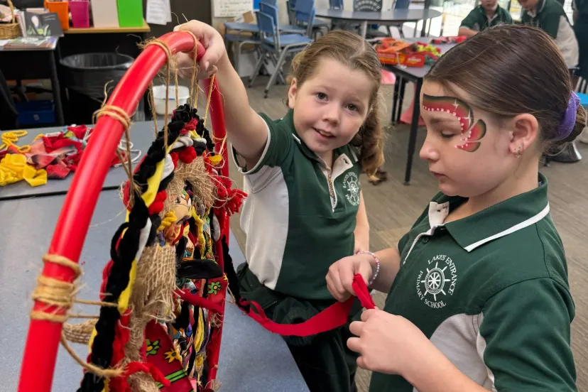 Two students weaving fabric strips through a hoop in class