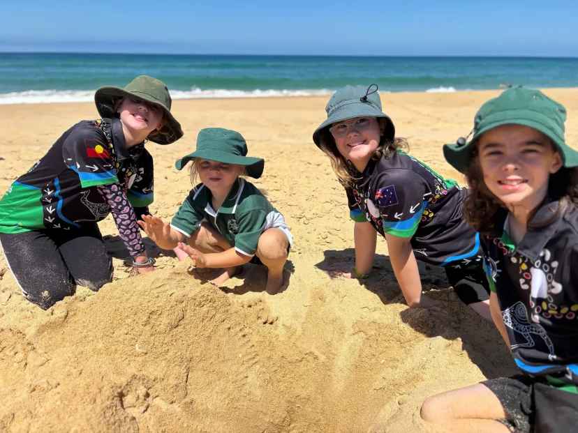 Four students in school bucket hats digging in the sand at the beach