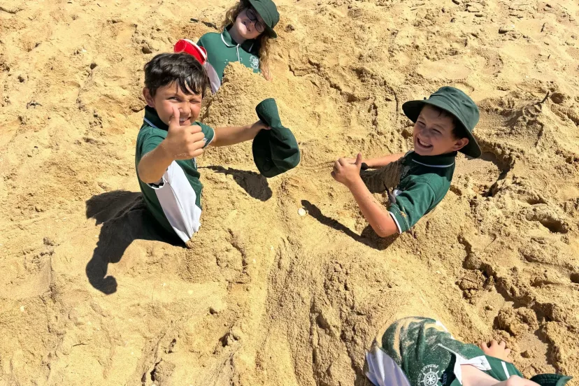 Students buried up to their shoulders in beach sand, laughing