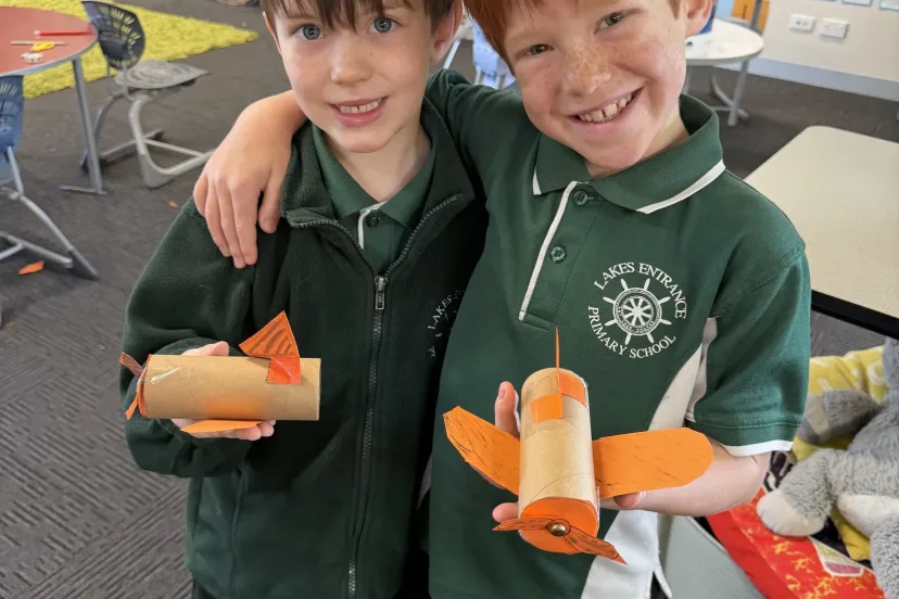 Two students with their arms round each other holding model planes they built