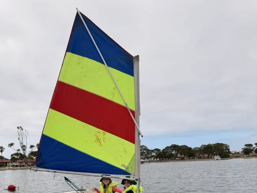 A school sailing dinghy under a striped sail on the lake